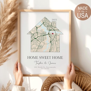 May include: A framed print with a house-shaped map design, a red heart, and the text "HOME SWEET HOME." The print includes the names "Taylor & James," the year "2025," and an address in Portsmouth, VA. The frame is light brown.