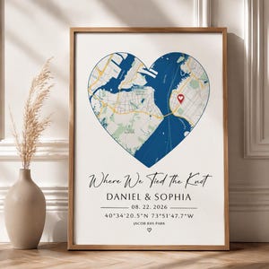 Puede incluir: Una lámina enmarcada con un mapa en forma de corazón de una zona costera con un marcador de ubicación rojo. Debajo del mapa, el texto dice: Where We Tied the Knot, DANIEL & SOPHIA, 22.08.2026, 40°34'20.5"N 73°51'47.7"W, JACOB RIIS PARK, y un pequeño corazón.