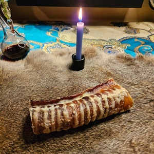 Può includere: Un lungo osso da masticare marrone e secco su una superficie pelosa marrone. Una candela blu accesa è sullo sfondo.