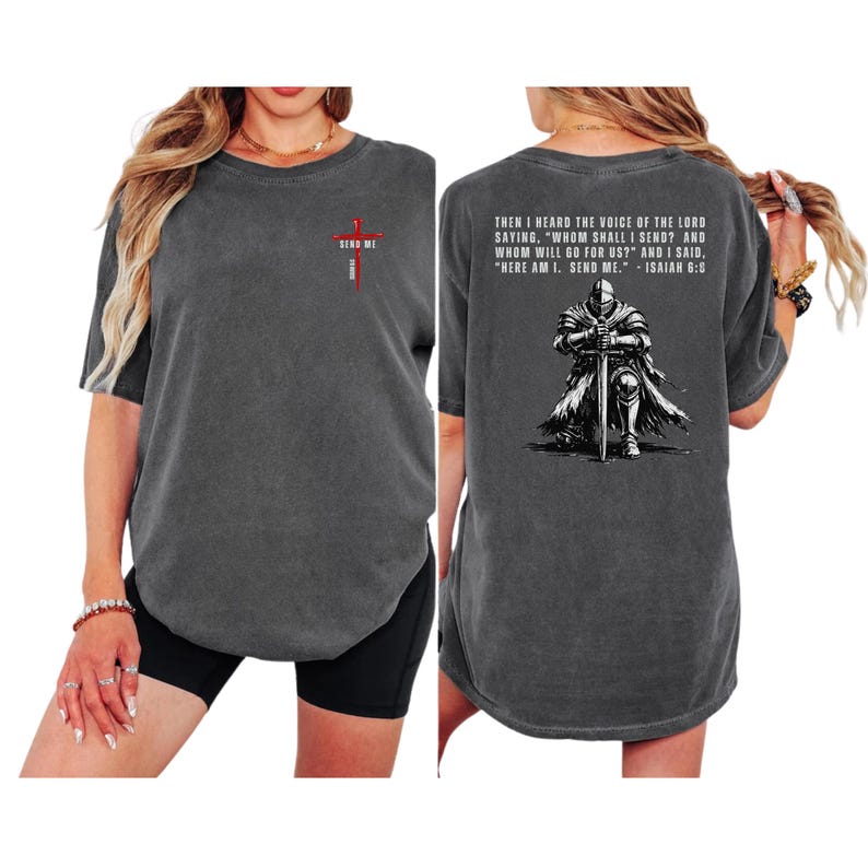 May include: A charcoal gray short-sleeve t-shirt featuring a small red cross graphic on the front chest with the text "SEND ME". The back displays a graphic of a knight kneeling with a sword and the text "THEN I HEARD THE VOICE OF THE LORD..."