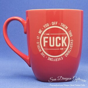 May include: A red ceramic mug with a large handle. The mug features the word "FUCK" in a white circle, surrounded by text. The mug has the text "Sea Dragon Giftware" at the bottom.