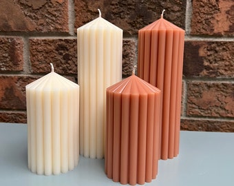 Puede incluir: Cuatro velas pilares, dos son de color marrón claro y dos son de color crema. Las velas son todas acanaladas y tienen una forma de estrella en la parte superior.