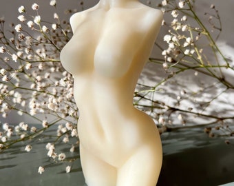 May include: A white, candle shaped like a human torso. The candle is sitting on a light blue surface.