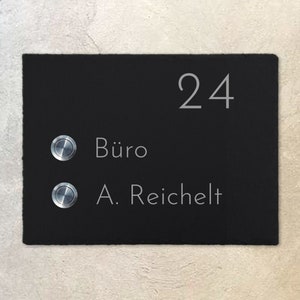 Può includere: Un cartello in ardesia nera con il numero 24, due pulsanti del campanello e il testo "Büro" e "A.  Reichelt".