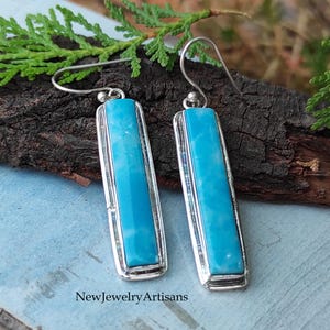 May include: A pair of silver dangle earrings with rectangular turquoise stones. The stones have a light blue color with white veins.
