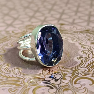 May include: A silver ring with a large, oval-shaped amethyst gemstone. The ring has a simple, elegant design with a band that wraps around the finger multiple times.