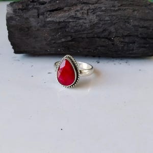 Könnte beinhalten: Ein silberner Ring mit einem tropfenförmigen roten Edelstein.