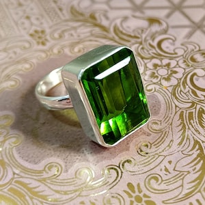 May include: A silver ring with a large, emerald green gemstone set in a rectangular shape.