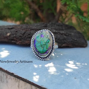 May include: A silver ring with a green, purple, and white iridescent oval stone set in a twisted silver band.