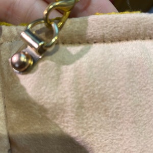 K&ouml;nnte beinhalten: Eine goldfarbene Kette mit einem Verschluss, der an einer beigefarbenen Stoffoberfl&auml;che befestigt ist.