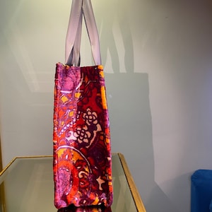 May include: A red, orange, and purple paisley patterned tote bag with light gray handles.