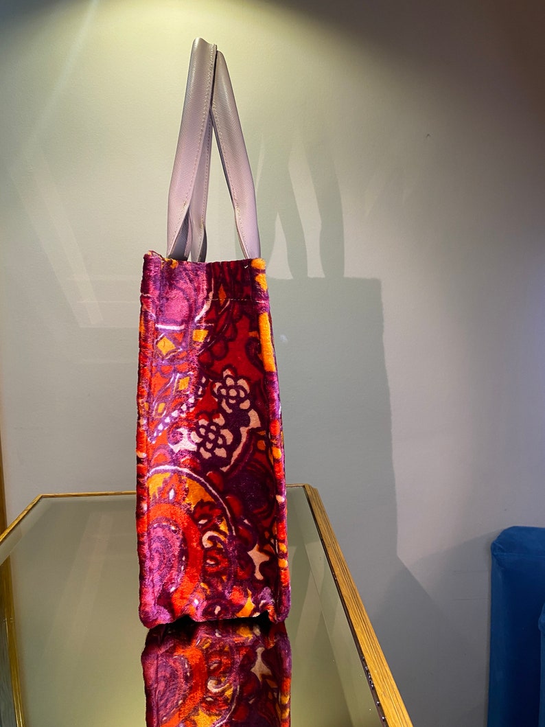 May include: A red, orange, and purple paisley patterned tote bag with light gray handles.