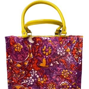 May include: A purple, red, and yellow floral patterned tote bag with a yellow leather handle.