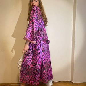 May include: A long, pink and black patterned robe with a sash. The robe is made of a silky material and has a relaxed fit.