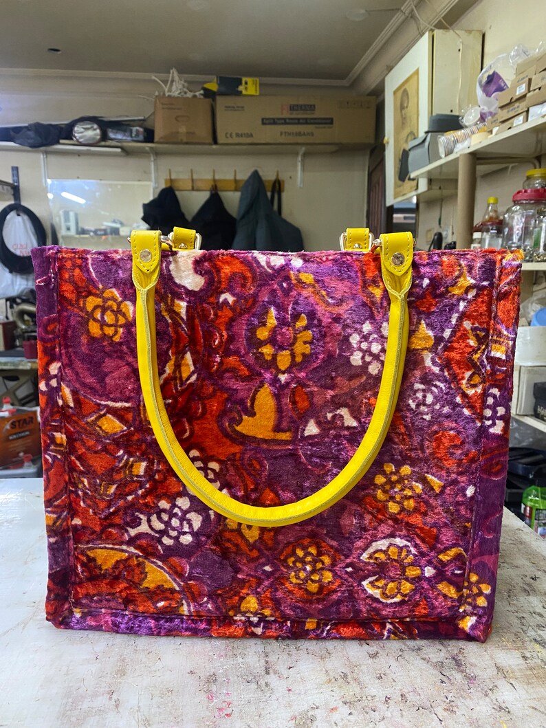 May include: A large tote bag with yellow handles. The bag is made of a purple, orange, and yellow fabric with a floral pattern.