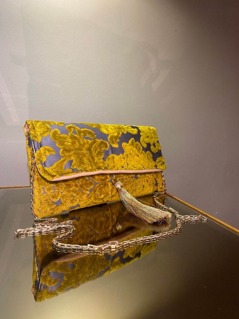 K&ouml;nnte beinhalten: Eine goldene Kettenhandtasche mit Quaste und Blumenmuster. Die Tasche ist aus weichem, samtigem Material.