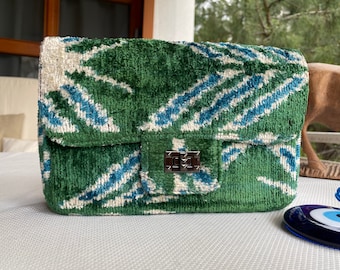 May include: A green, blue, and white patterned velvet handbag with a silver clasp.