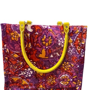 May include: A purple, red, and orange patterned tote bag with yellow leather handles.