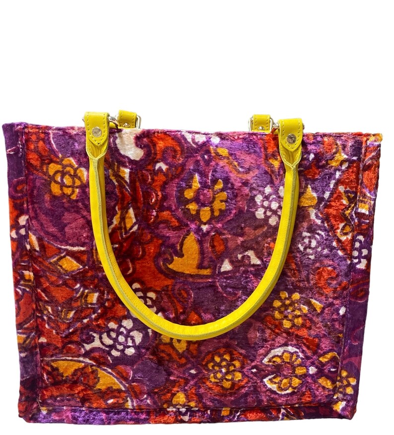 May include: A purple, red, and orange patterned tote bag with yellow leather handles.
