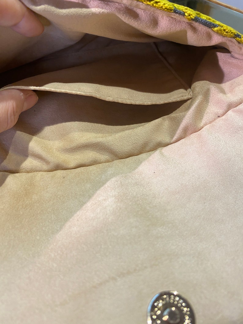 K&ouml;nnte beinhalten: Das Innere einer beige Stofftasche mit einer kleinen Tasche und einem silbernen Metallverschluss.