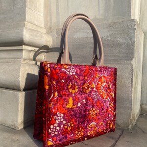 May include: A red, orange, and white patterned tote bag with a beige leather handle.