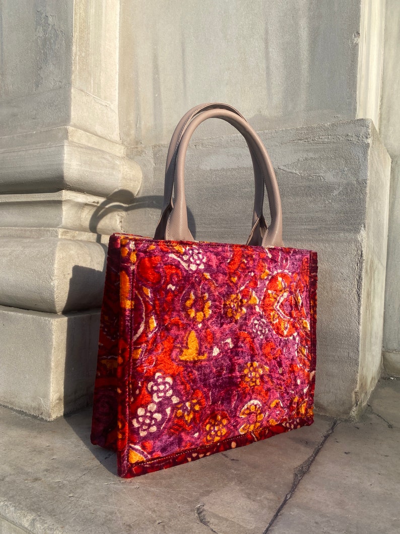 May include: A red, orange, and white patterned tote bag with a beige leather handle.