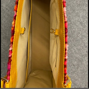 May include: A yellow faux fur tote bag with a red, orange, and pink trim. The bag has a zipper closure and a small interior pocket. The bag is open and the interior is visible.