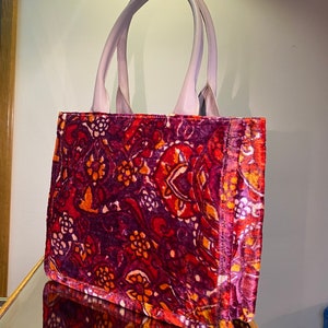 May include: A purple tote bag with a red, orange, and purple floral pattern. The bag has two handles.