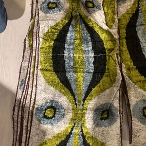 May include: A pair of decorative fabric panels with a repeating pattern. The design features large, stylized shapes in shades of green, black, and blue on a cream background. The panels have a soft, velvety texture and are likely used for curtains or upholstery.