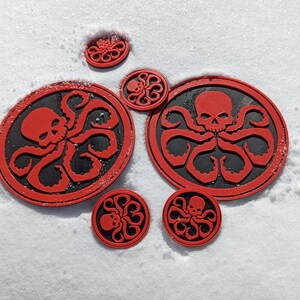 Puede incluir: Ocho pegatinas circulares rojas y negras con un dise&ntilde;o de calavera y pulpo. Las pegatinas est&aacute;n sobre una superficie blanca.
