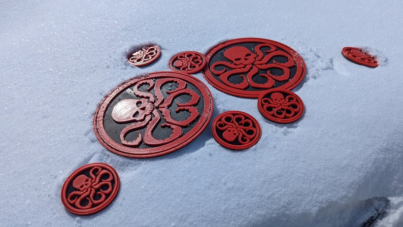 Puede incluir: Una colecci&oacute;n de pegatinas circulares rojas y negras con un dise&ntilde;o de calavera y pulpo, colocadas sobre una superficie blanca nevada.