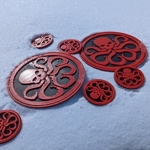 Puede incluir: Un conjunto de ocho pegatinas circulares rojas y negras con un dise&ntilde;o de calavera y tent&aacute;culos. Las pegatinas est&aacute;n sobre una superficie blanca nevada.