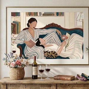 Peut inclure: Une impression d'art encadrée représentant deux figures sur un canapé bleu canard, l'une lisant, l'autre tenant une fleur. Un chat est à proximité. Une table présente une bouteille de vin, des verres, un arrangement floral et un petit arbre en pot. L'œuvre est dans un cadre doré.