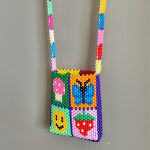May include: A colorful beaded crossbody bag with a matching strap. The bag features a square design with a mushroom, butterfly, smiley face, and strawberry. The strap and bag are made of small, colorful beads.