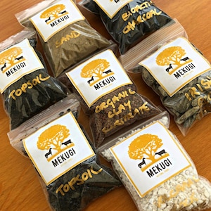 Pode incluir: Oito pequenos sacos de plástico transparente cheios de diferentes tipos de solo e meios de cultivo. Os sacos são etiquetados com as palavras "Mekugi", "Terra vegetal", "Areia", "Substrato de argila orgânica", "Carvão bioativo" e "Musgo irlandês".