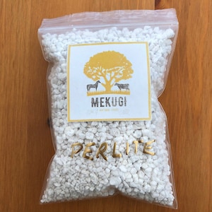 Pode incluir: Um saco de plástico transparente cheio de perlita branca, um vidro vulcânico leve e poroso. O saco tem um rótulo com o texto "MEKUQI NATURAL GOODS" e um logotipo de uma árvore com dois animais. O texto "PERLITE" está escrito em letras douradas no saco.