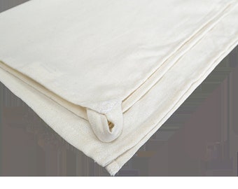 May include: Folded off-white canvas tote bag with a loop handle. The bag is made of a thick, durable material and appears to be new. The corner of the bag is visible, showing the stitching and construction.