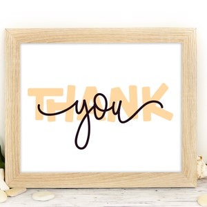 May include: A framed print with the text "THANK you" in a peach color with black cursive writing.