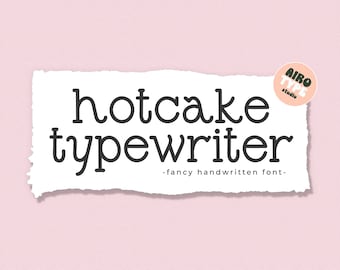 以下が含まれることがあります： 破れた縁のある白い紙に、「hotcake typewriter」というテキストが黒い手書きのフォントで書かれています。テキストの後に、より小さなフォントで「fancy handwritten font」と続きます。右上の角には、「AIRO TYPE studio」というテキストが書かれた丸いステッカーがあります。