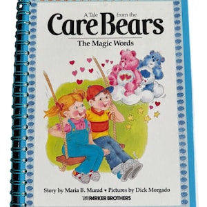 May include: A blue book with a spiral binding titled "A Tale from the Care Bears The Magic Words". The cover features an illustration of two children on a swing with Care Bears in the background.