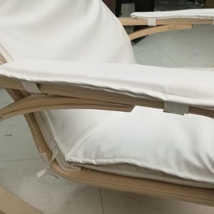 May include: A modern wooden rocking chair with a light wood frame and white cushions. The chair features curved armrests and a padded seat and backrest. The white cushions are secured with fabric straps.