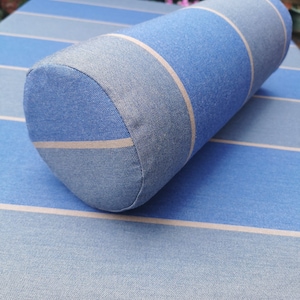 May include: A cylindrical bolster cushion in shades of blue and white, with a striped pattern. The cushion is made of a textured fabric and is placed on a matching blue and white striped surface. The cushion is approximately 30 cm long.
