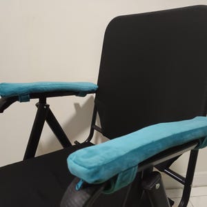 May include: A black folding chair with teal armrests. The chair has a black fabric seat and back.