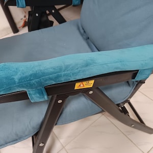Puede incluir: Una silla plegable azul con un marco de metal negro y un reposabrazos de terciopelo azul. La silla tiene una etiqueta de advertencia en el reposabrazos que dice "Precaución: No se pare en la silla."