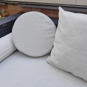 May include: A close-up of a gray and white patterned outdoor furniture cushion. The cushion is made of a soft, textured fabric and has a round shape.