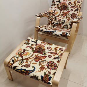 Pode incluir: Uma cadeira de balanço de madeira e um otomano com almofadas de padrão floral. As almofadas têm um fundo creme com um design floral colorido.