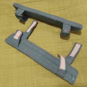 May include: Two pairs of blue fabric armrests with pink straps. The armrests are made of a soft, textured fabric and have a simple design.