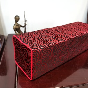 May include: A red and black rectangular cushion with a swirling pattern. The cushion is made of a soft, plush fabric and has a red trim.