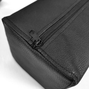 May include: Black leather zippered pouch with a textured surface.