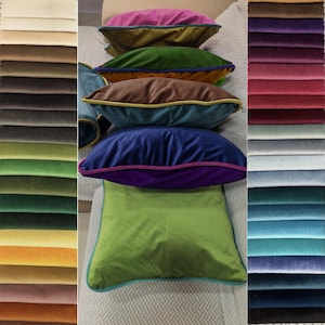 Pode incluir: Uma pilha de almofadas decorativas de veludo coloridas em tons de rosa, verde, castanho, azul e verde limão. Cada almofada tem uma borda contrastante. Amostras de tecido em várias cores são visíveis à esquerda e à direita da imagem.